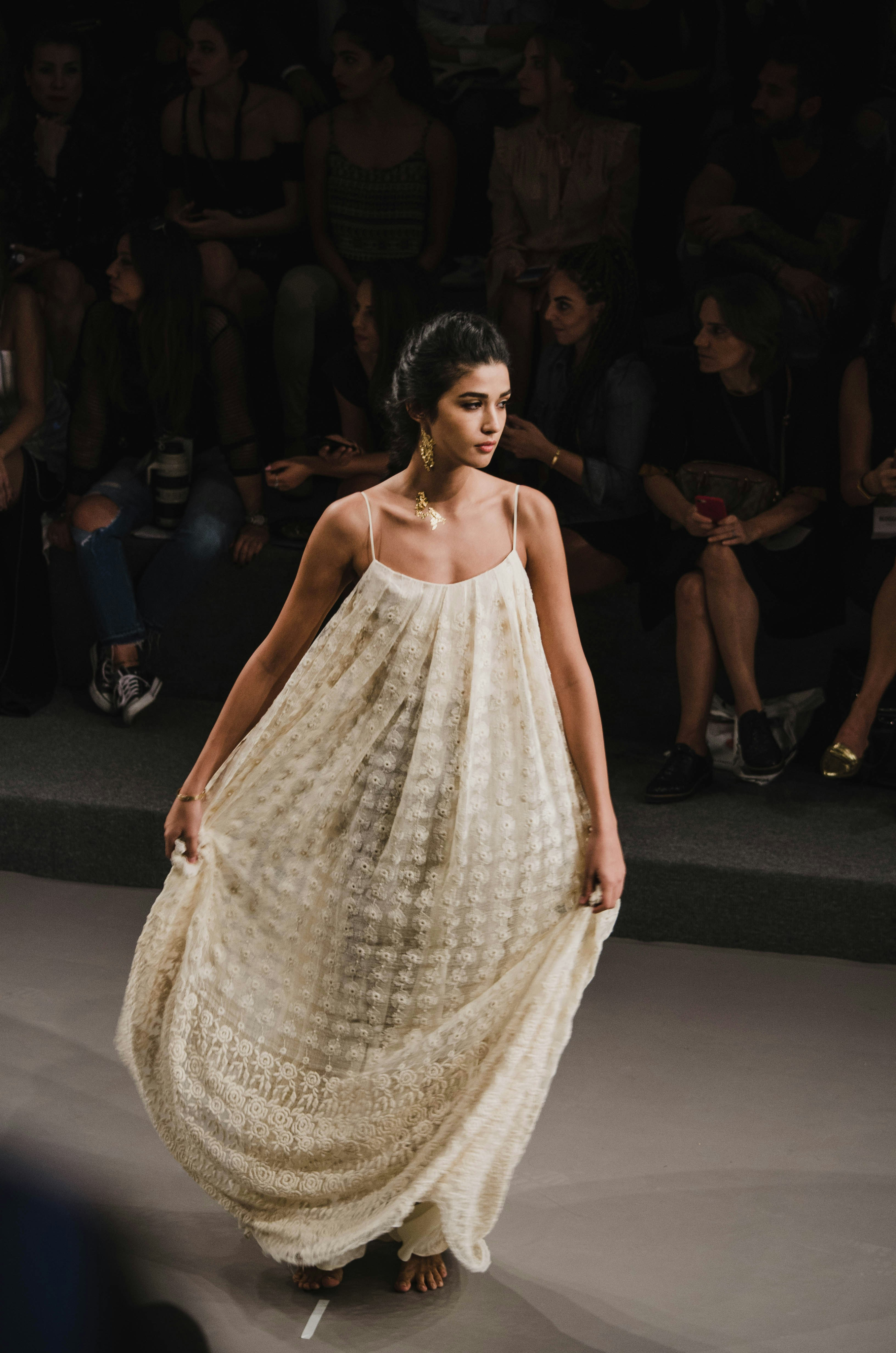 Woman in white dress and gold earrings walking down runway
